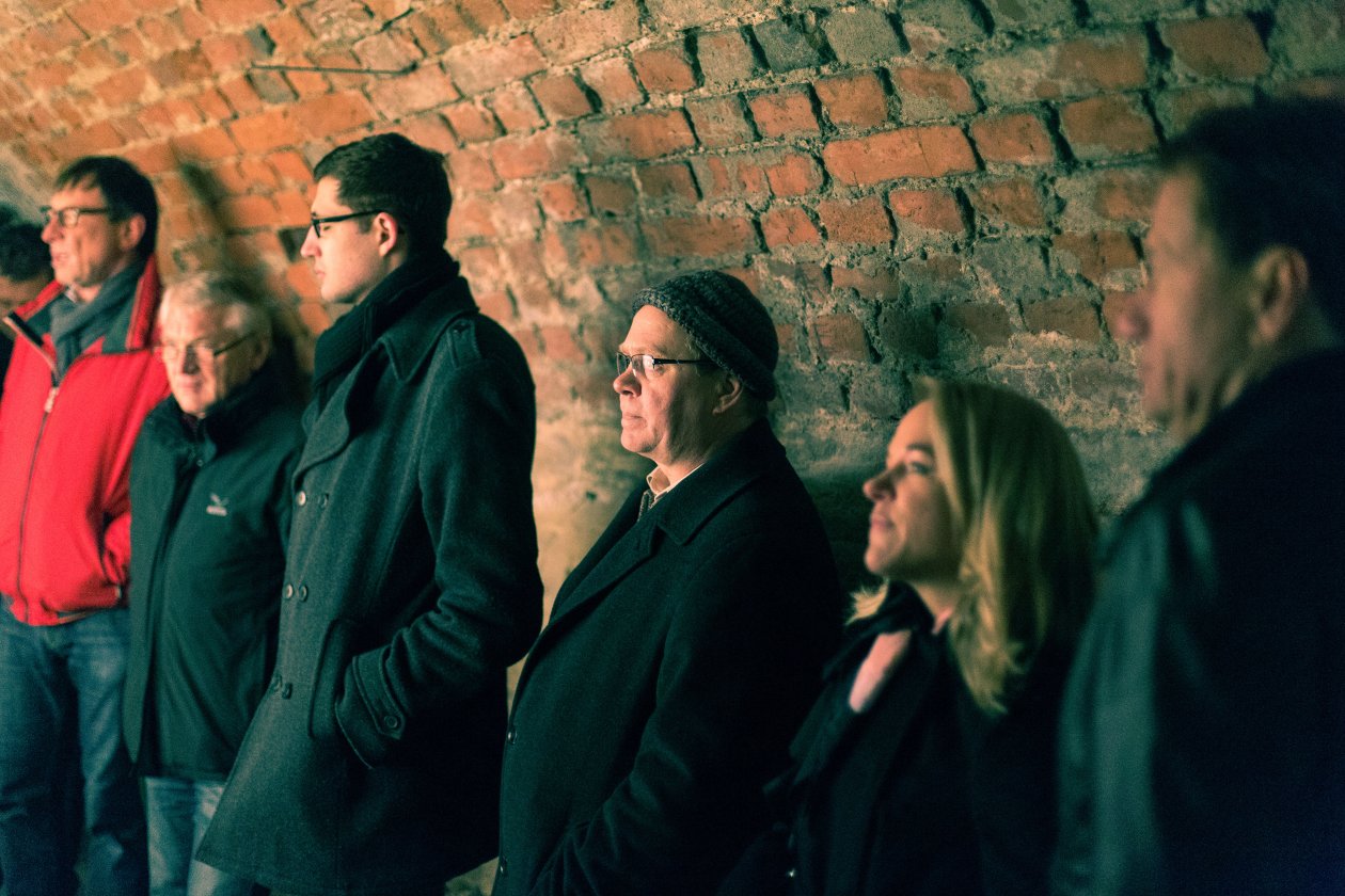 Several people wearing winter jackets are standing next to a wall.