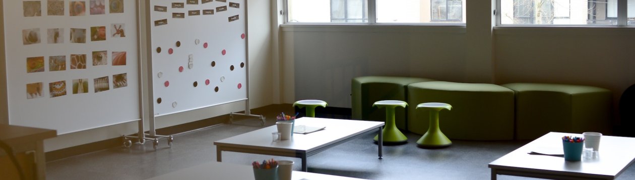 A classroom with several tables and chairs. On the wall there are two magnetic boards with pictures on them.