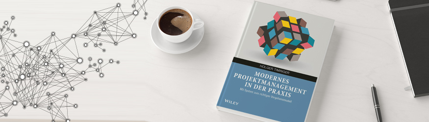 Ein Buch mit dem Titel Modernes Projektmanagement in der Praxis und eine Tasse Kaffee.