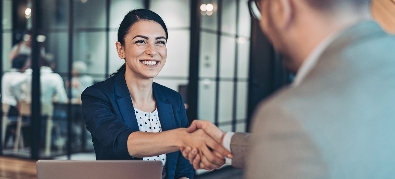 A woman with black hair smiles and shakes hands with a man.