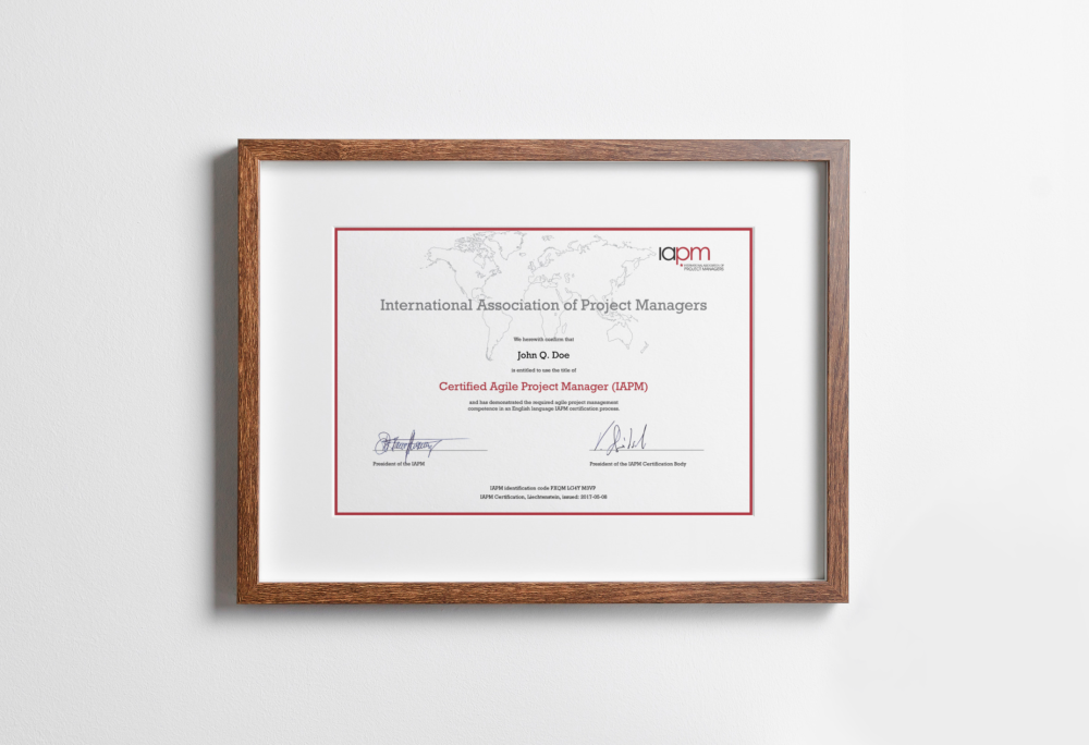 The Certified Agile Project Manager certificate is in a wood-coloured picture frame and hangs on a wall.