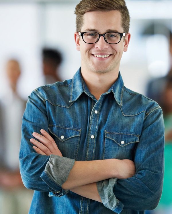 A brown-haired man with glasses wears a denim shirt, he smiles at the camera.