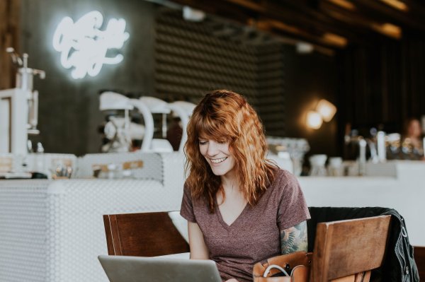 A red-haired woman works on her laptop and smiles.