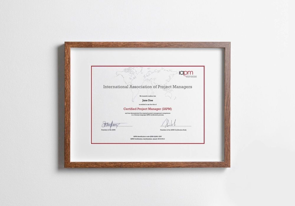 The Certified Project Manager certificate is in a wood-coloured picture frame and hangs on a wall.