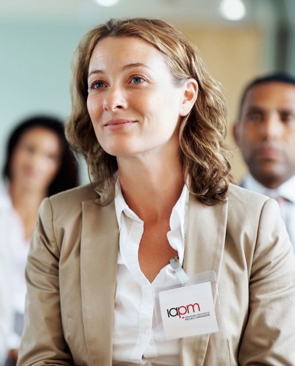 A light brown-haired woman wears a white blouse and a beige blazer, she smiles.