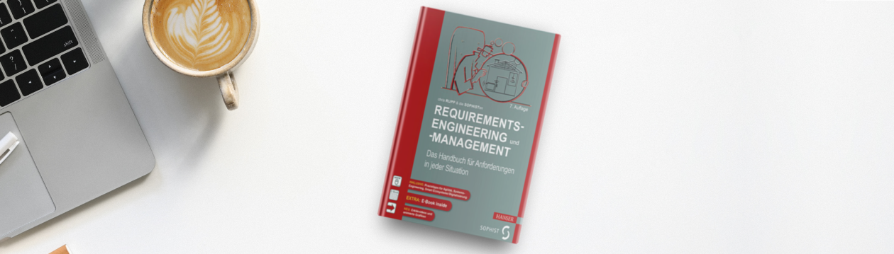 Chris Rupps Buch "Requirements-Engineering und -Management" liegt auf einem Tisch neben einem Laptop und einem Cappuccino 