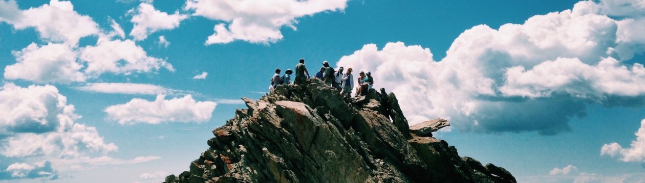 Conflict Management - People on a rock formation under a white, cloudy sky.