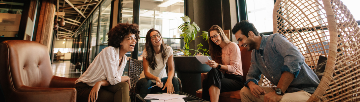 Four colleagues laugh in a modern office.