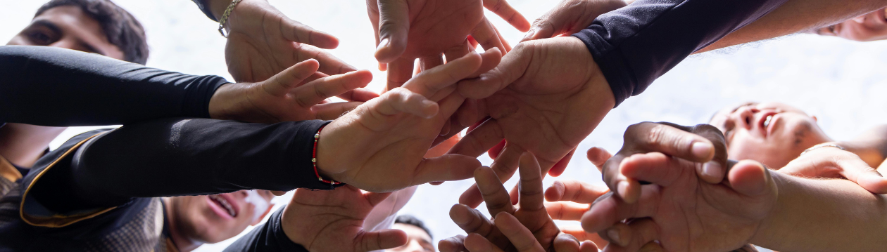 Mehrere Menschen stehen im Kreis und strecken ihre Hände zur Mitte übereinander. Die Aufnahme ist von unten fotografiert und zeigt ein Team, das Zusammenhalt, Zusammenarbeit und Gemeinschaft symbolisiert. Mehrere Menschen stehen im Kreis und strecken ihre Hände zur Mitte übereinander. Die Aufnahme ist von unten fotografiert und zeigt ein Team, das Zusammenhalt, Zusammenarbeit und Gemeinschaft symbolisiert.