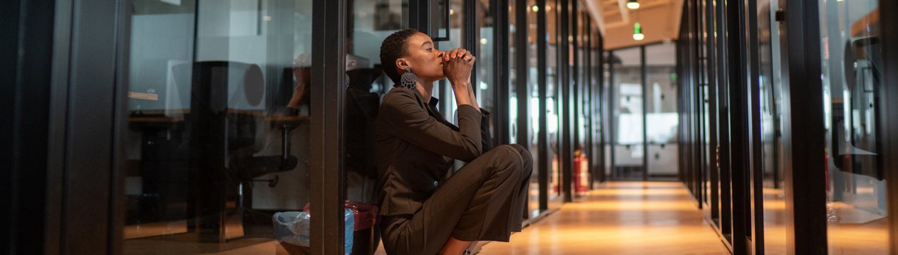 Woman sitting in a long hallway with her hands folded in front of her mouth.