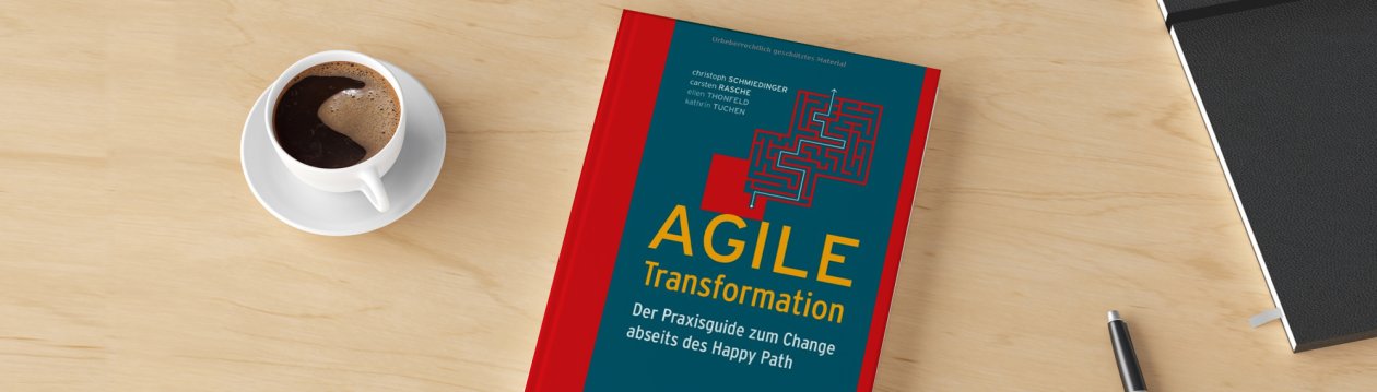 Auf einem Tisch liegt das Buch "Agile Transformation", daneben sind eine Tasse Kaffee, ein Stift und ein Notizbuch zu sehen