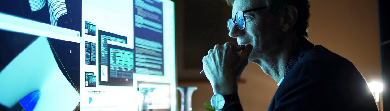 Man with glasses looking at computer screen with charts on it.