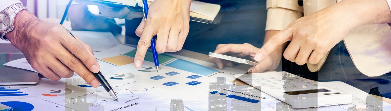 Several hands hold a calculator, a pencil and point to printed graphs and tables