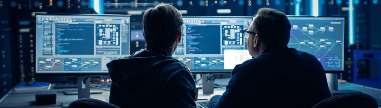 Two men can be seen from behind, sitting in front of monitors with lines of code.