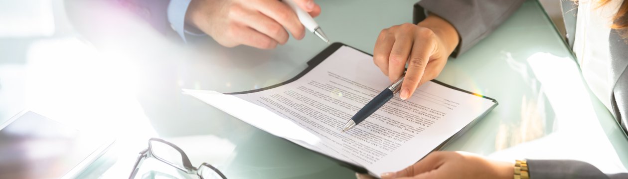 A contract and the hands of two people pointing at the contract with ballpoint pens are shown in cut-out form.