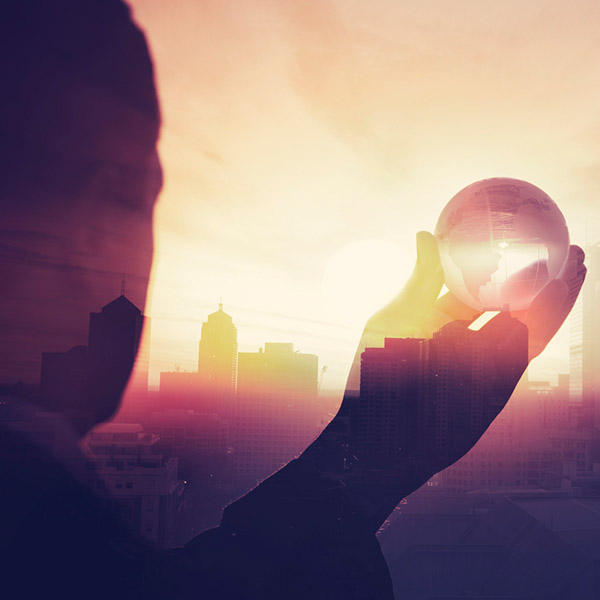 Man holding transparent globe in his hand towards the sun. In the background a skyline.