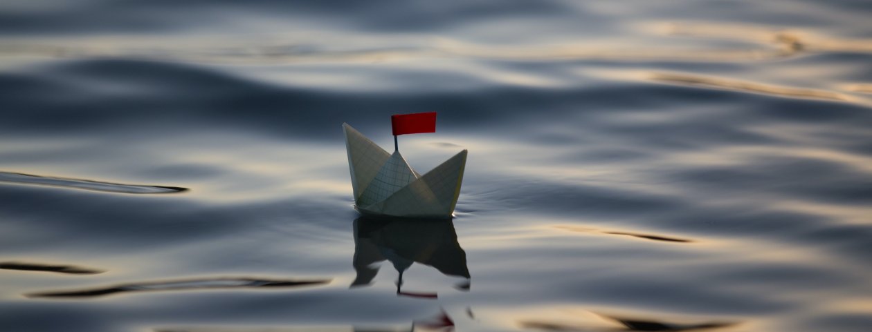 Ein Papierschiffchen auf dem Wasser mit einer roten Flagge.