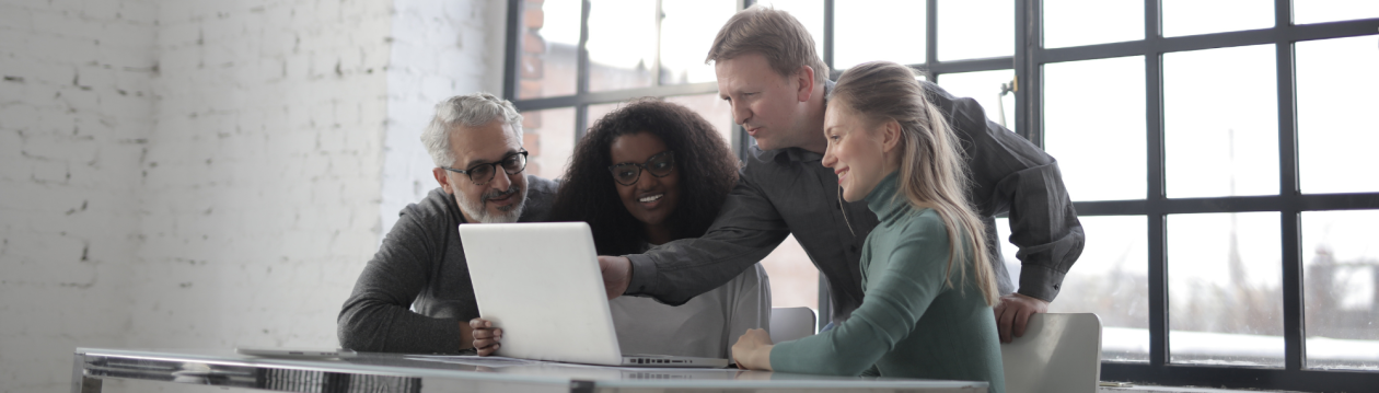Mehrere Personen sitzen an einem Laptop, eine Person zeigt auf diesen Laptop. Mehrere Personen sitzen an einem Laptop, eine Person zeigt auf diesen Laptop.