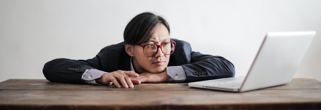 Man rests his face on one hand and looks at a laptop, waiting.