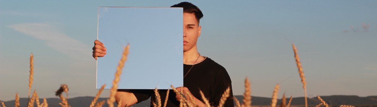 A man holds a mirror in front of his face. A man holds a mirror in front of his face.