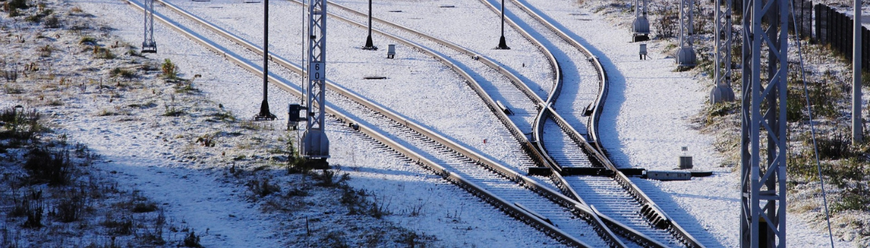 Verschneite Bahngleise mit mehreren Weichen und Stahlmasten auf einem offenen Gelände.