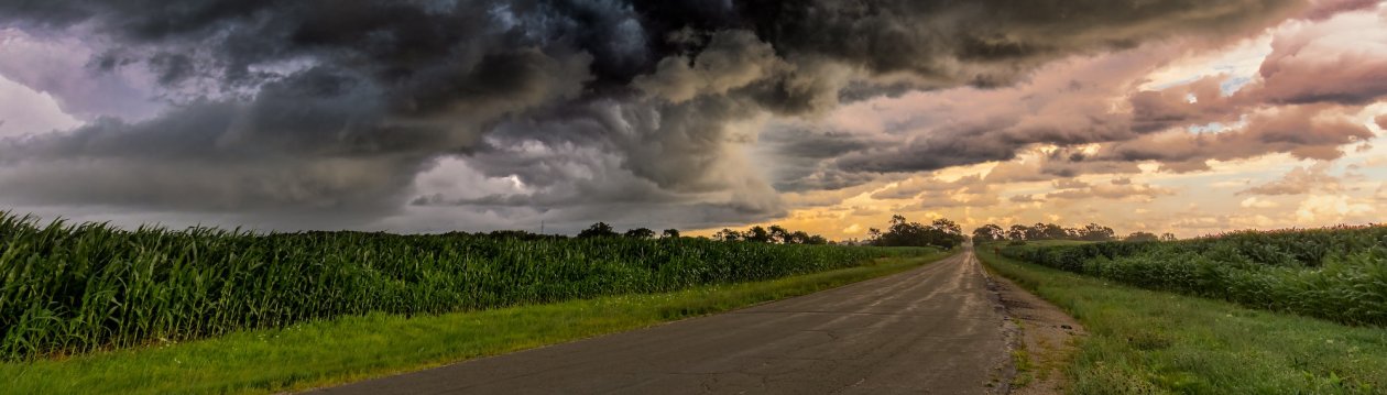 A road with storm clouds above. In the background, the clouds are dissipating. 