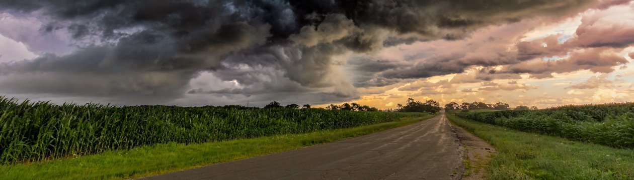 A road with storm clouds above. In the background, the clouds are dissipating. A road with storm clouds above. In the background, the clouds are dissipating.