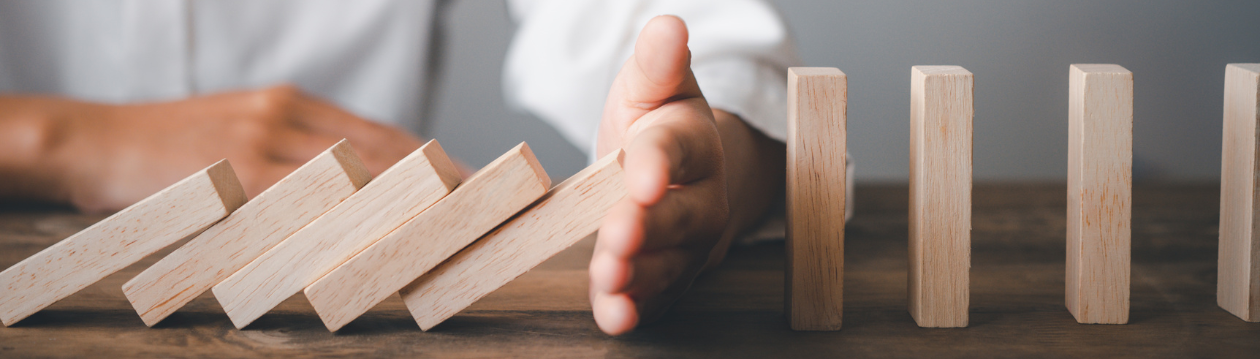 A hand stops a row of falling wooden blocks standing on a wooden table. A hand stops a row of falling wooden blocks standing on a wooden table.