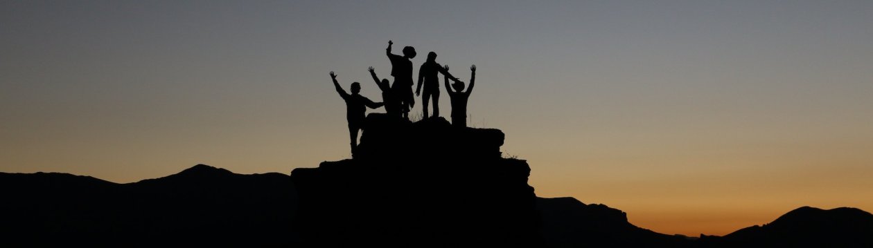Teambildung - Auf einem Berg stehen mehrere Silhouetten. Teambildung - Auf einem Berg stehen mehrere Silhouetten.