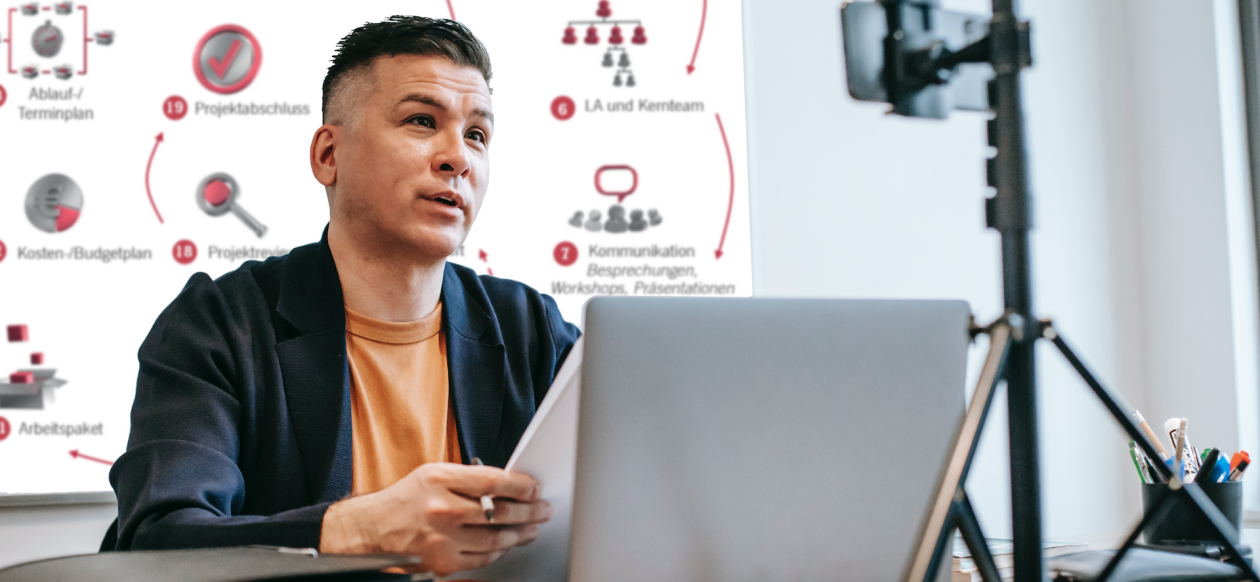 Mann sitzt vor einer Kamera. Im Hintergrund sieht man den Projektatlas der IAPM. Mann sitzt vor einer Kamera. Im Hintergrund sieht man den Projektatlas der IAPM.