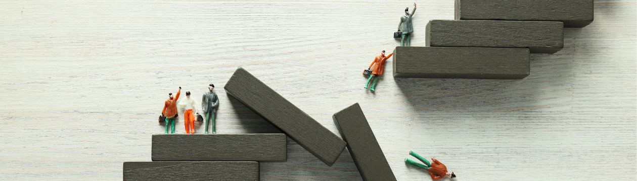 The picture shows miniature figures on unstable stacked blocks, with some figures falling and others standing.