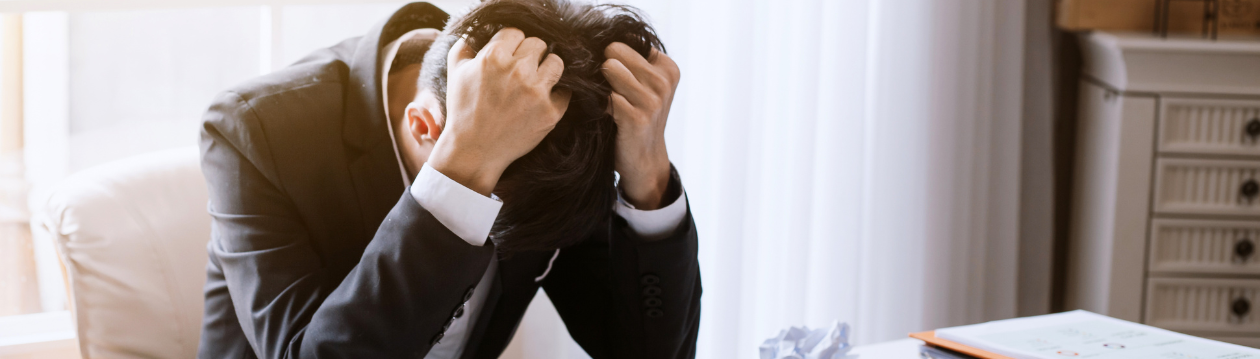 Ein Mann im Anzug sitzt verzweifelt an seinem Schreibtisch und hat die Hände in den Haaren. Ein Mann im Anzug sitzt verzweifelt an seinem Schreibtisch und hat die Hände in den Haaren.